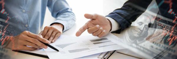 Two professionals reviewing financial documents with charts and graphs, overlaid with imagery of currency and stock market data.